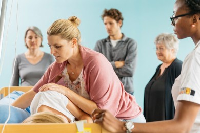 Pflegehelferin zeigt Kursteilnehmenden am Krankenbett den Umgang mit einer Patientin. 
