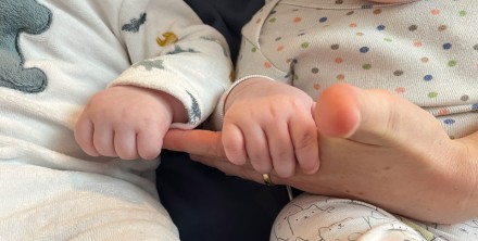 Eine erwachsene Hand hält die Hände von Zwillingsbabys