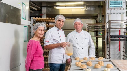 Die freiwillige Mentorin, ein Berufsausbildner und der erwachsene Lernende Hassan stehen in der Bäckerei.