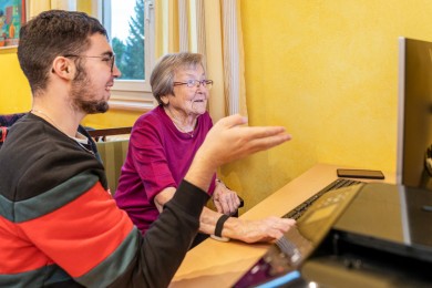 Ein Freiwilliger vom Jugendrotkreuz erklärt einer Bewohnerin etwas am Computer