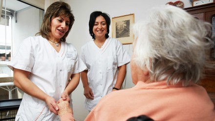 Zwei Pflegehelfende sprechen mit einer Bewohnenden in einem Alterszentrum.