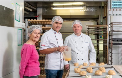 Die freiwillige Mentorin, ein Berufsausbildner und der erwachsene Lernende Hassan stehen in der Bäckerei.